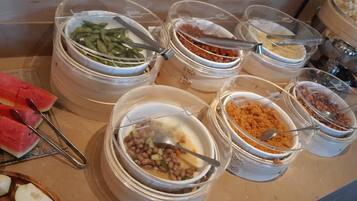 Een buffet met diverse gerechten, waaronder watermeloen, groene bonen en verschillende soorten bonen en granen.