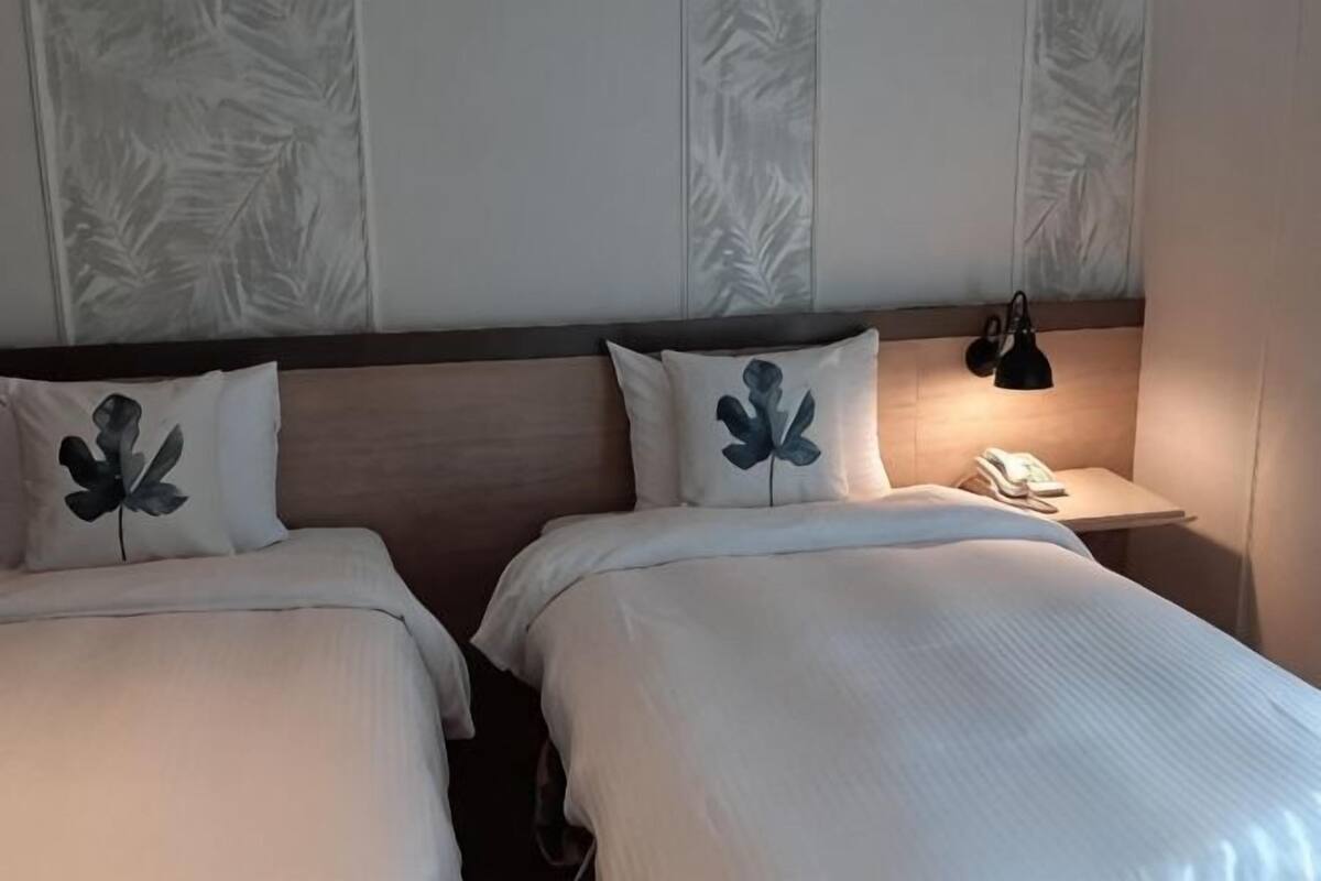 Une chambre d’hôtel avec deux lits, une table de chevet avec une lampe et un mur orné d’un motif de feuilles.