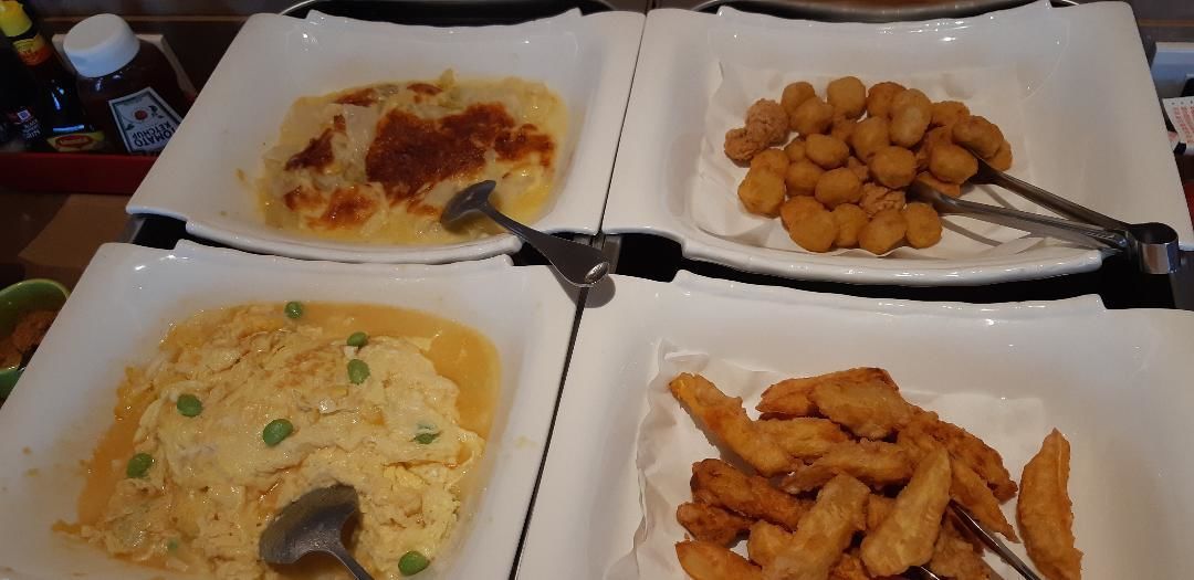 Four white plates with different dishes, including scrambled eggs, fried items, and a baked dish.