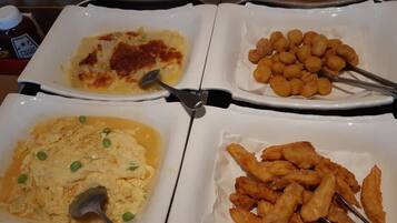 Four white plates with different dishes, including scrambled eggs, fried items, and a baked dish.