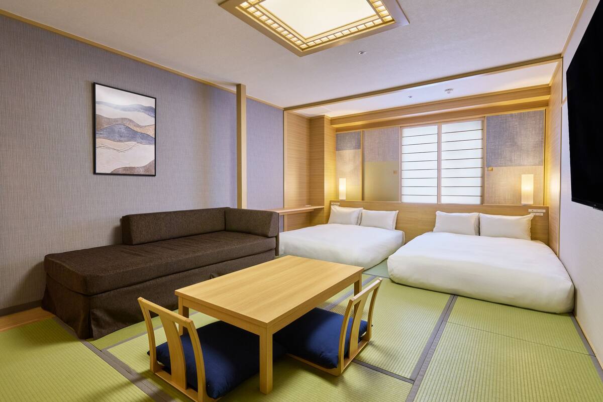 A room with a sofa, a bed, a table, and a futon.