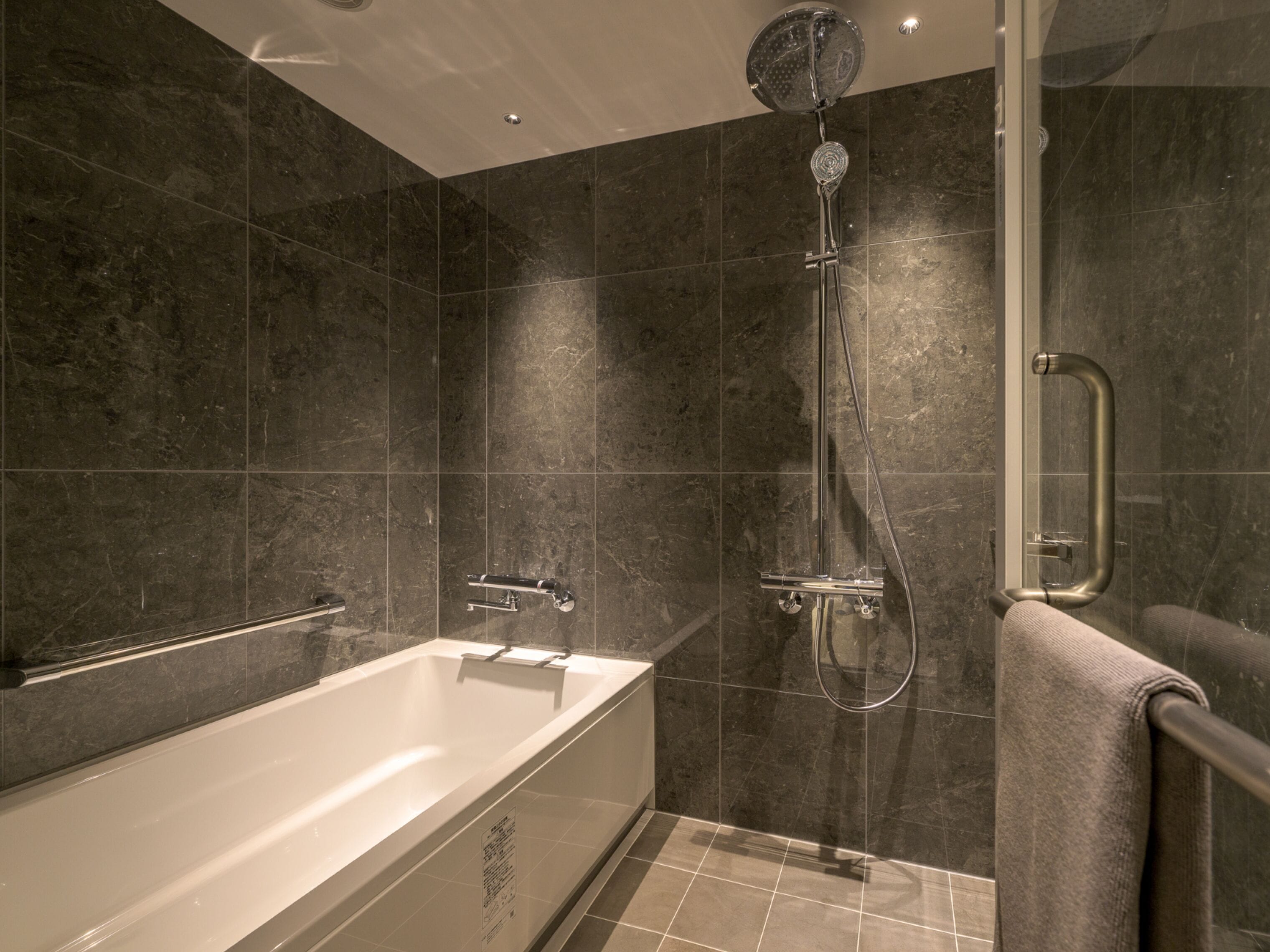 A modern bathroom with a bathtub, shower, and handrail.