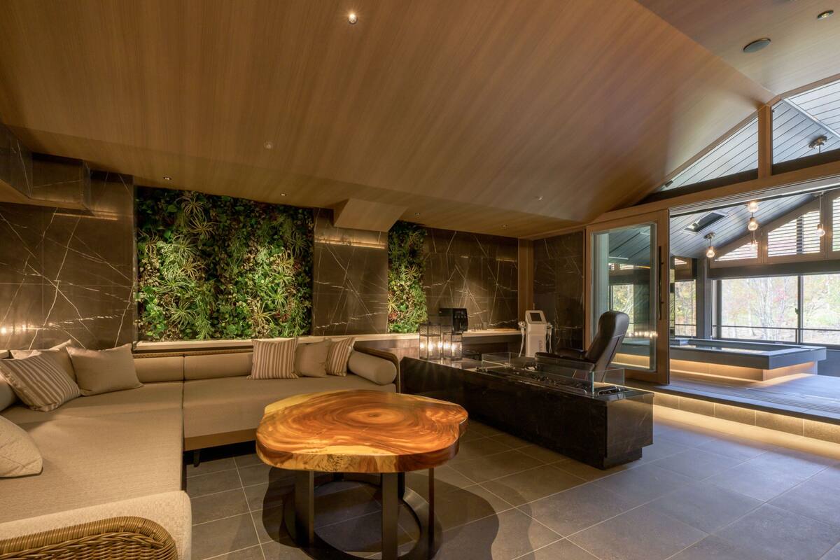 A modern living room with a wooden coffee table, a sofa, and a large window with a view of trees.