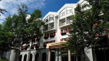 A multi-story hotel with a modern architectural design, featuring balconies with red shutters and a prominent entrance with a sign.