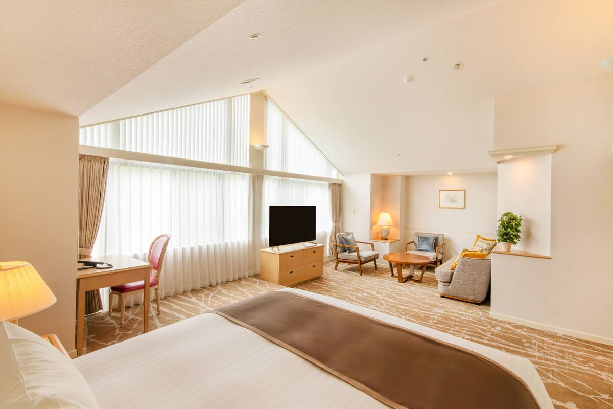 A hotel room with a large bed, a desk with a chair, a television, a sofa, and a small table.