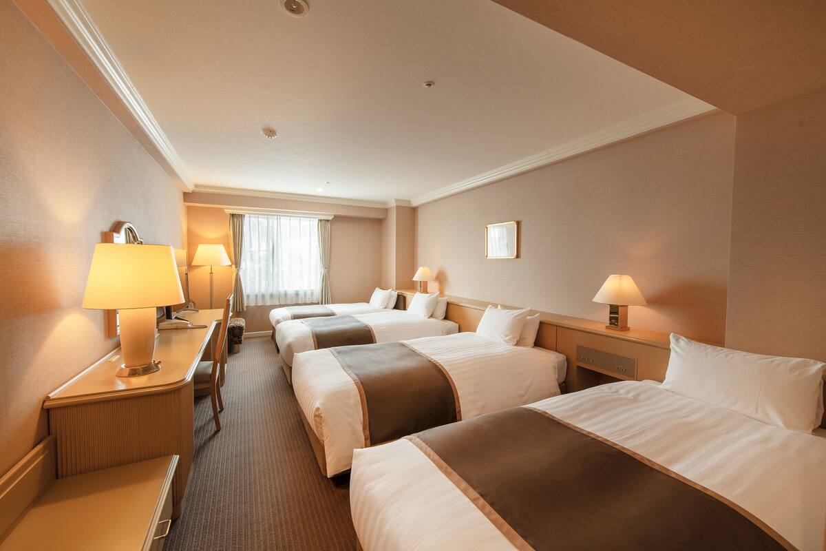 A hotel room with four beds, a desk, and two lamps.