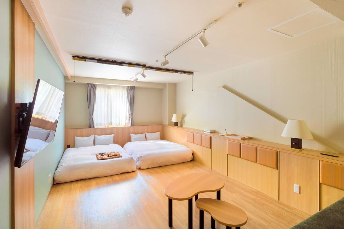 A hotel room with two beds, a desk, a chair, a TV, and a ceiling fan.