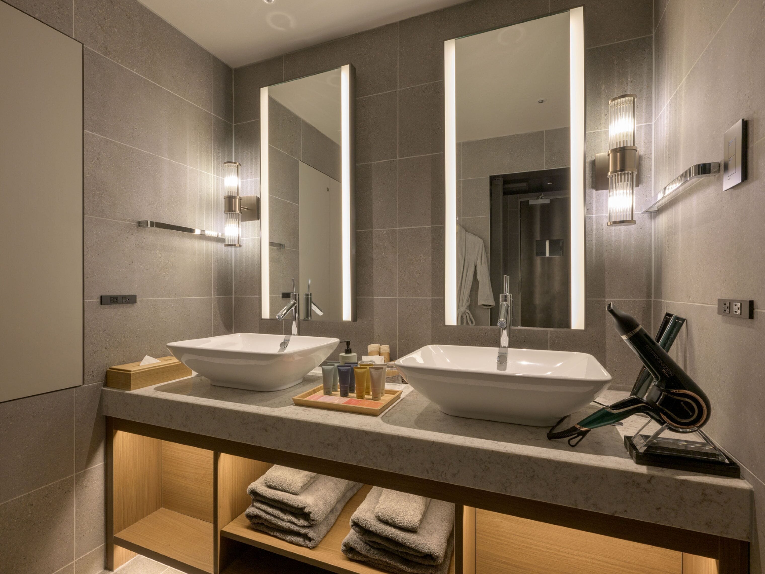 Une salle de bain moderne avec deux vasques sur pied, un grand miroir et un porte-serviettes.