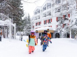 Uma rua coberta de neve com edifícios modernos, incluindo uma construção com várias andares e varandas.