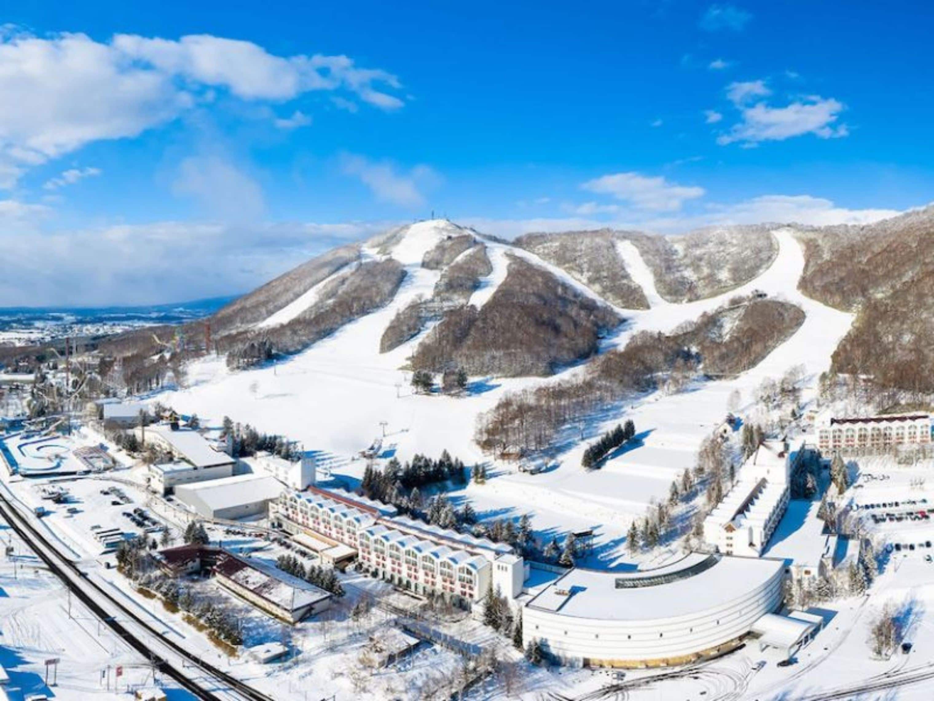 A snow-covered ski resort with a large building, ski slopes, and a mountain backdrop.