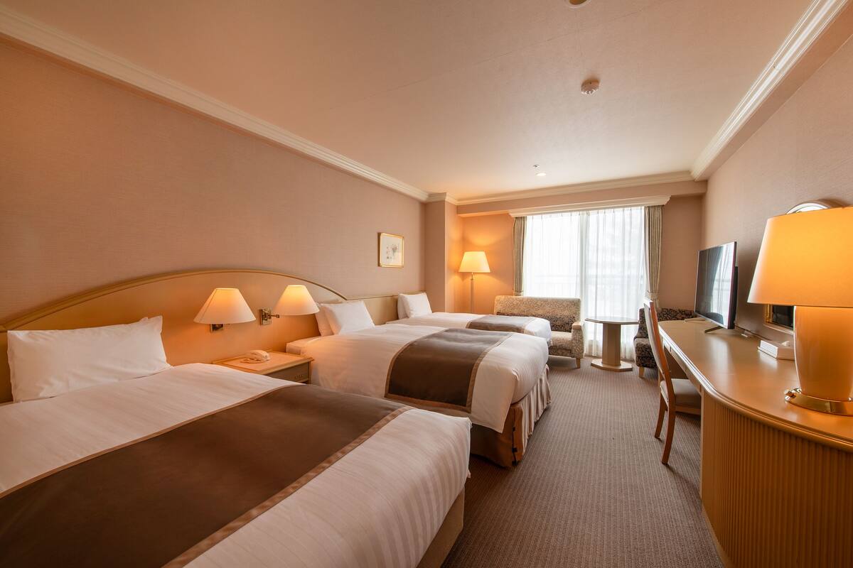A hotel room with two beds, a desk, a chair, and a television.