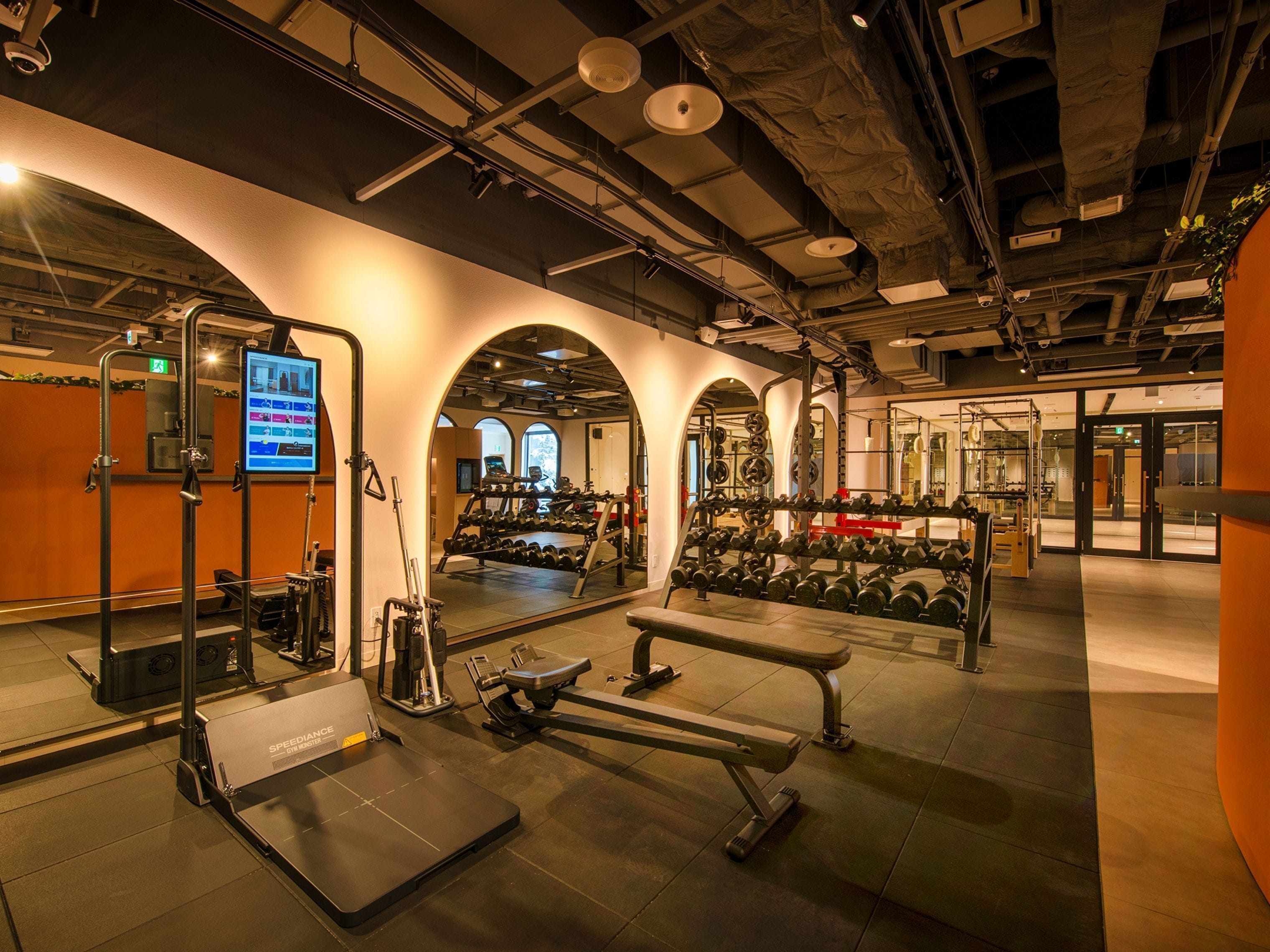 A gym with weightlifting equipment, treadmills, and a digital screen displaying workout information.