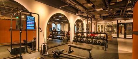 A gym with weightlifting equipment, treadmills, and a digital screen displaying workout information.