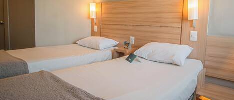 A hotel room with two single beds, each with a wooden headboard and bedside lamps.