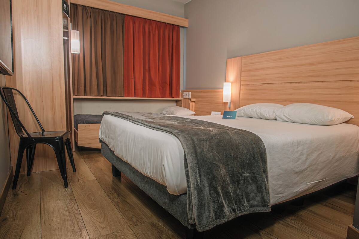 A hotel room with a bed, a desk, a chair, and a window with curtains.
