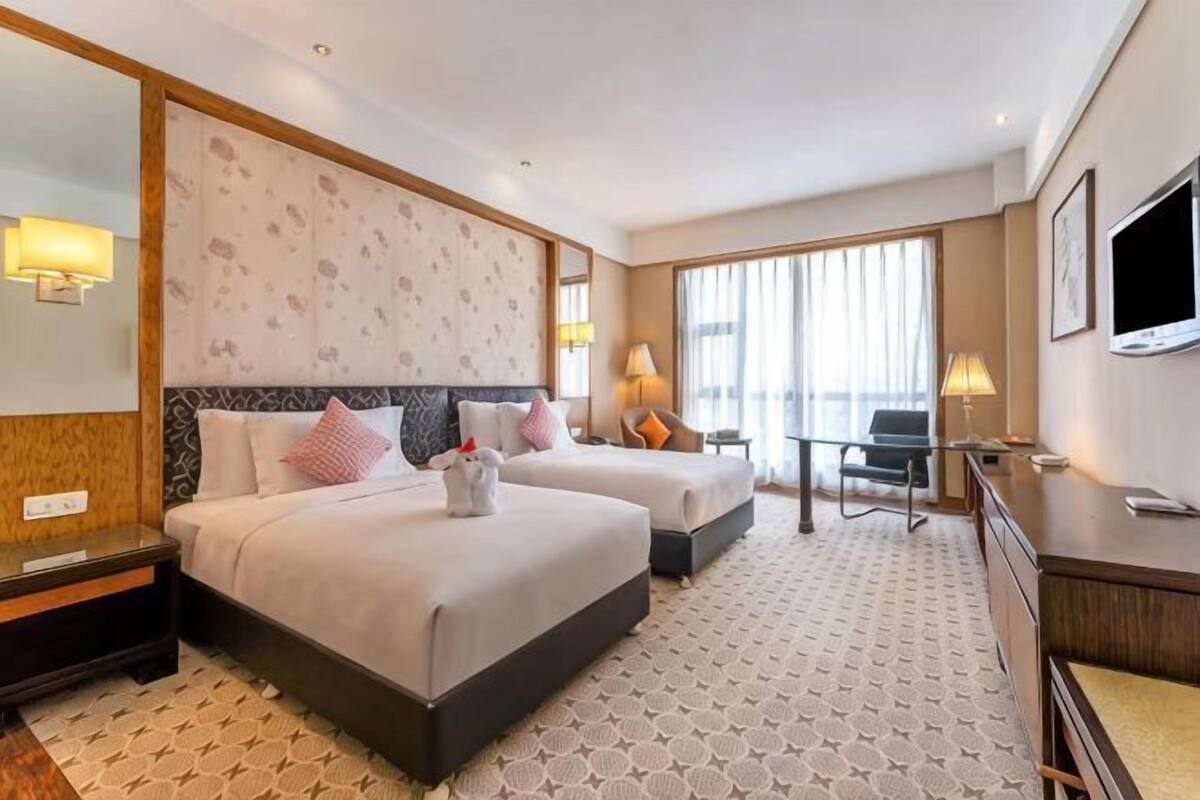 Een hotelkamer met twee bedden, een bureau, een stoel, een televisie en een groot raam.