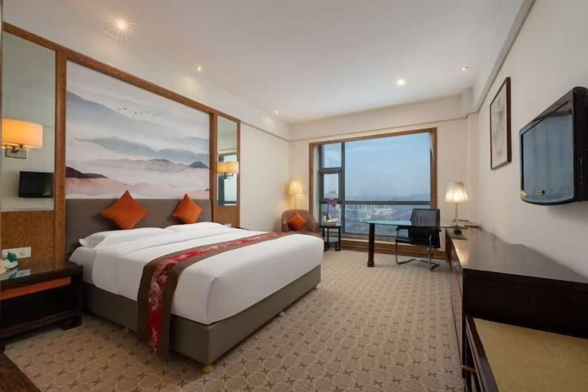 Een hotelkamer met een groot bed, twee kussens, een bureau, een stoel, een televisie en een groot raam met uitzicht.
