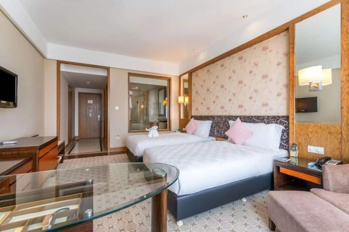 Een hotelkamer met twee bedden, een glazen tafel, een bank, een televisie en een spiegel.