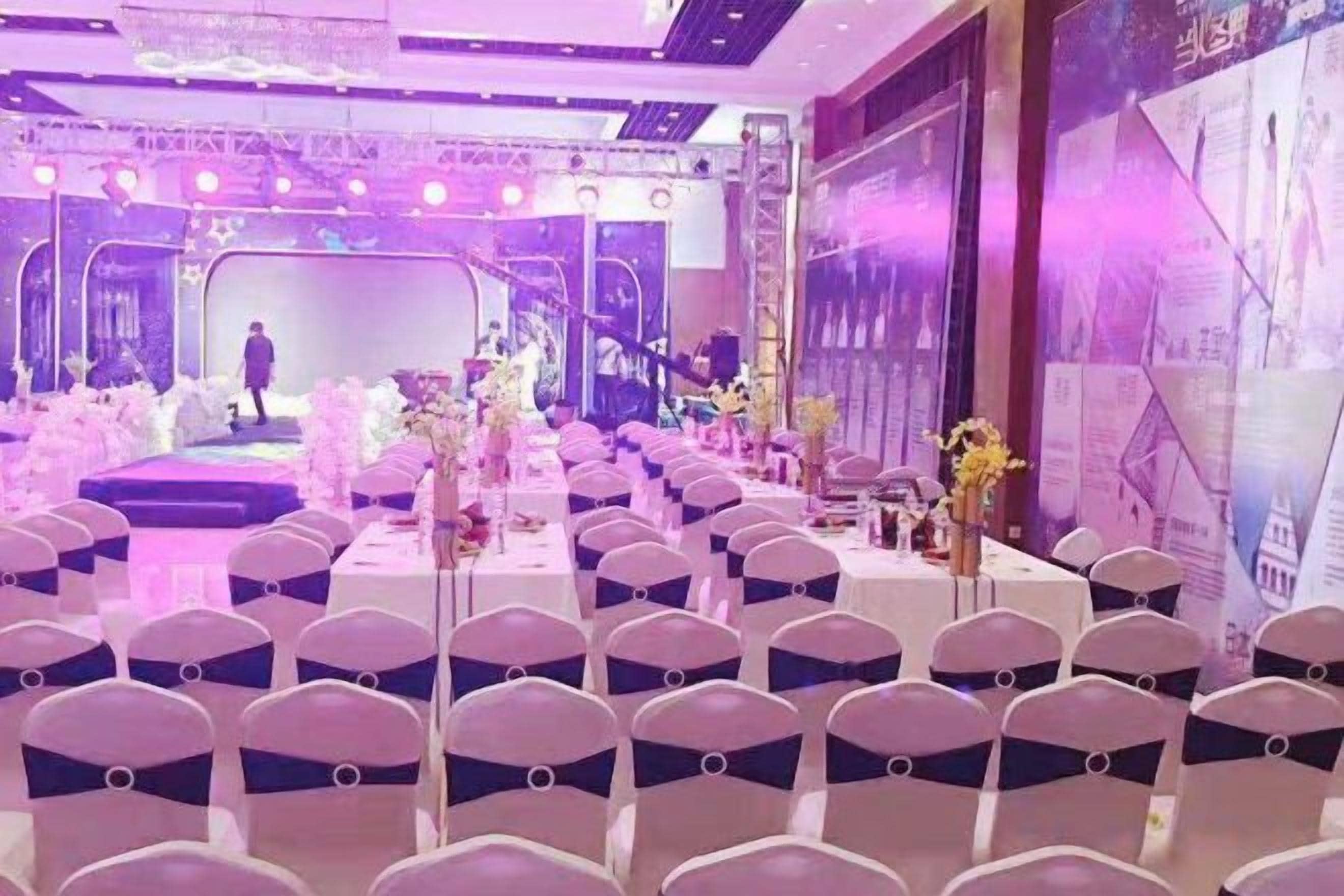 A banquet hall with rows of chairs, a stage, and a large screen.