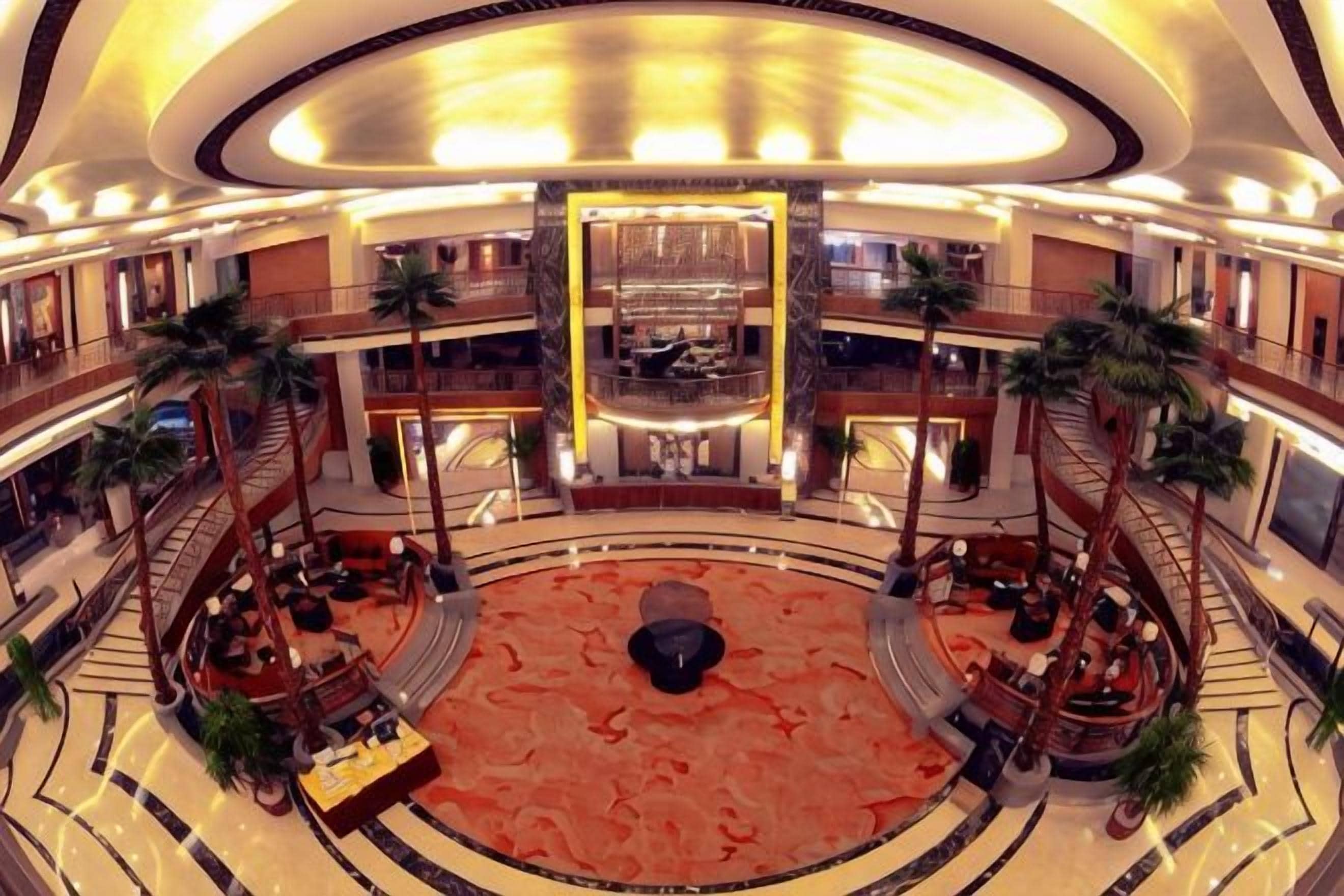 Un vestíbulo de hotel de varios niveles con un atrio central, palmeras y una zona de estar circular.