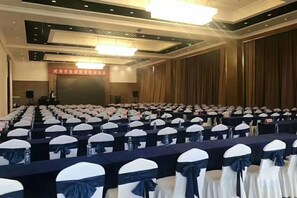 A conference room with rows of tables and chairs, a stage, and a banner on the wall. - Nishi Haitai Hotel (Weihai)