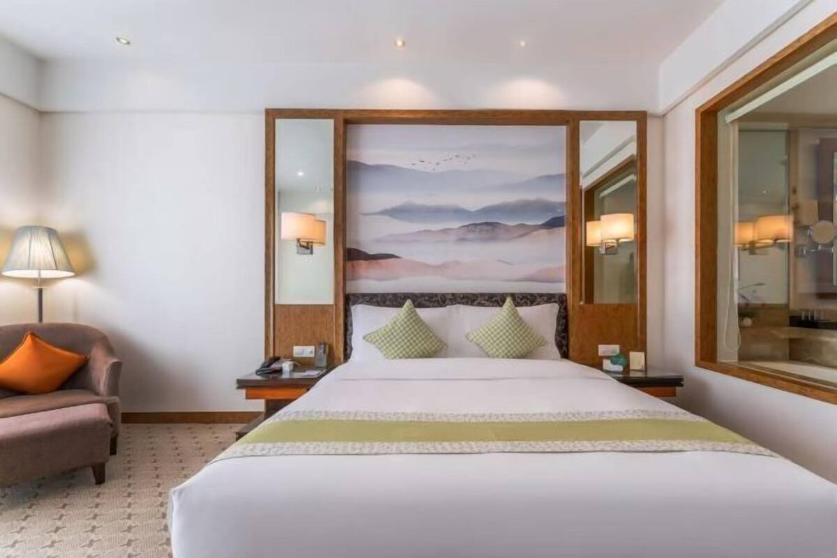 Een hotelkamer met een groot bed, een nachtkastje, een lamp, een stoel en een schilderij aan de muur.