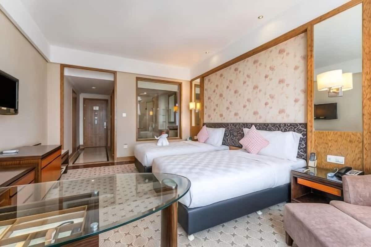 Een hotelkamer met twee bedden, een glazen tafel, een televisie, een spiegel en een groot raam.