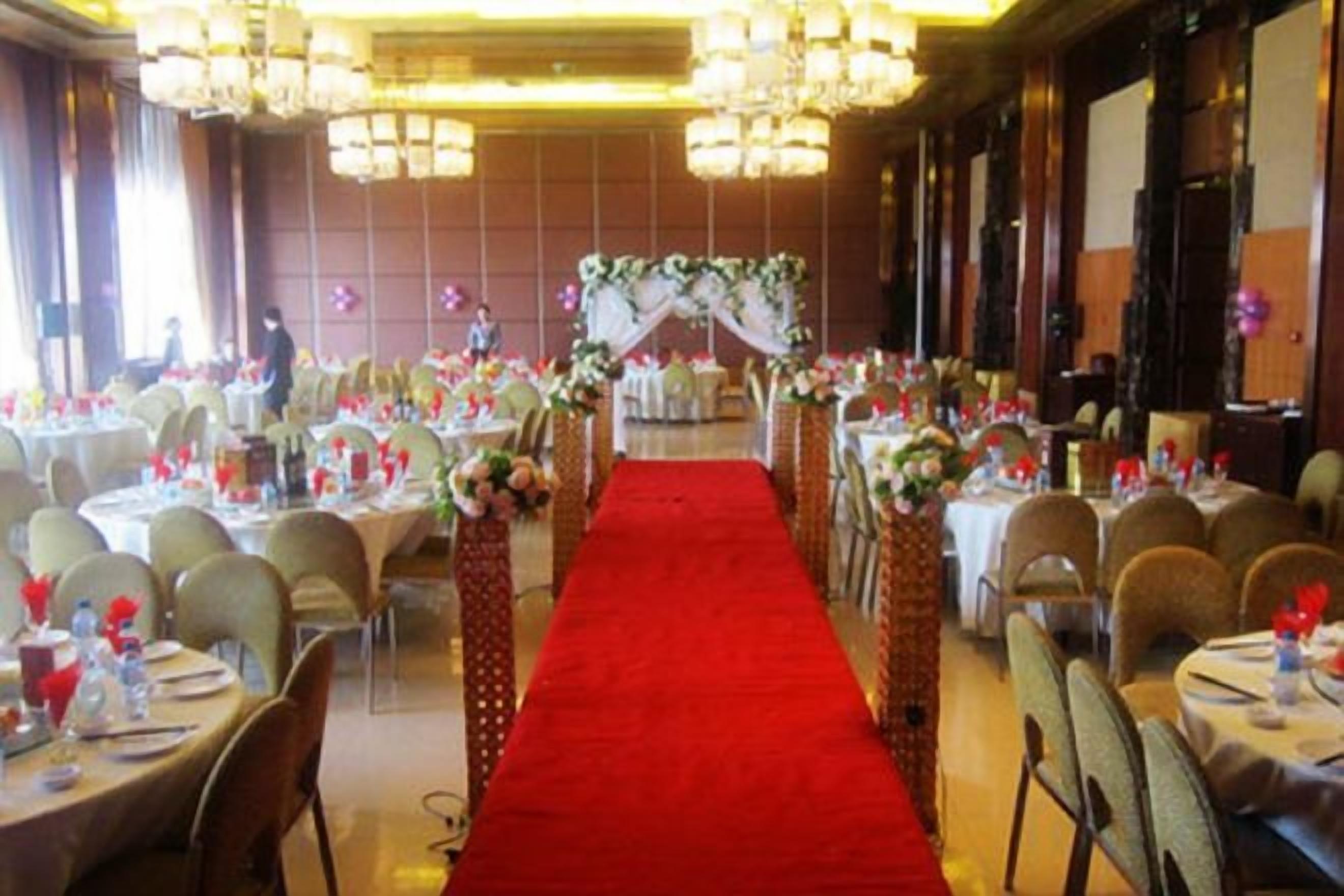 Un salón de banquetes con pasillo de alfombra roja, mesas redondas y candelabros.