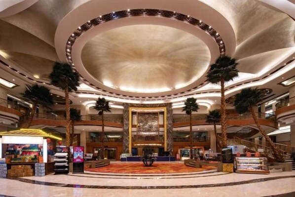 A spacious lobby with a central fountain, palm trees, and a grand staircase.