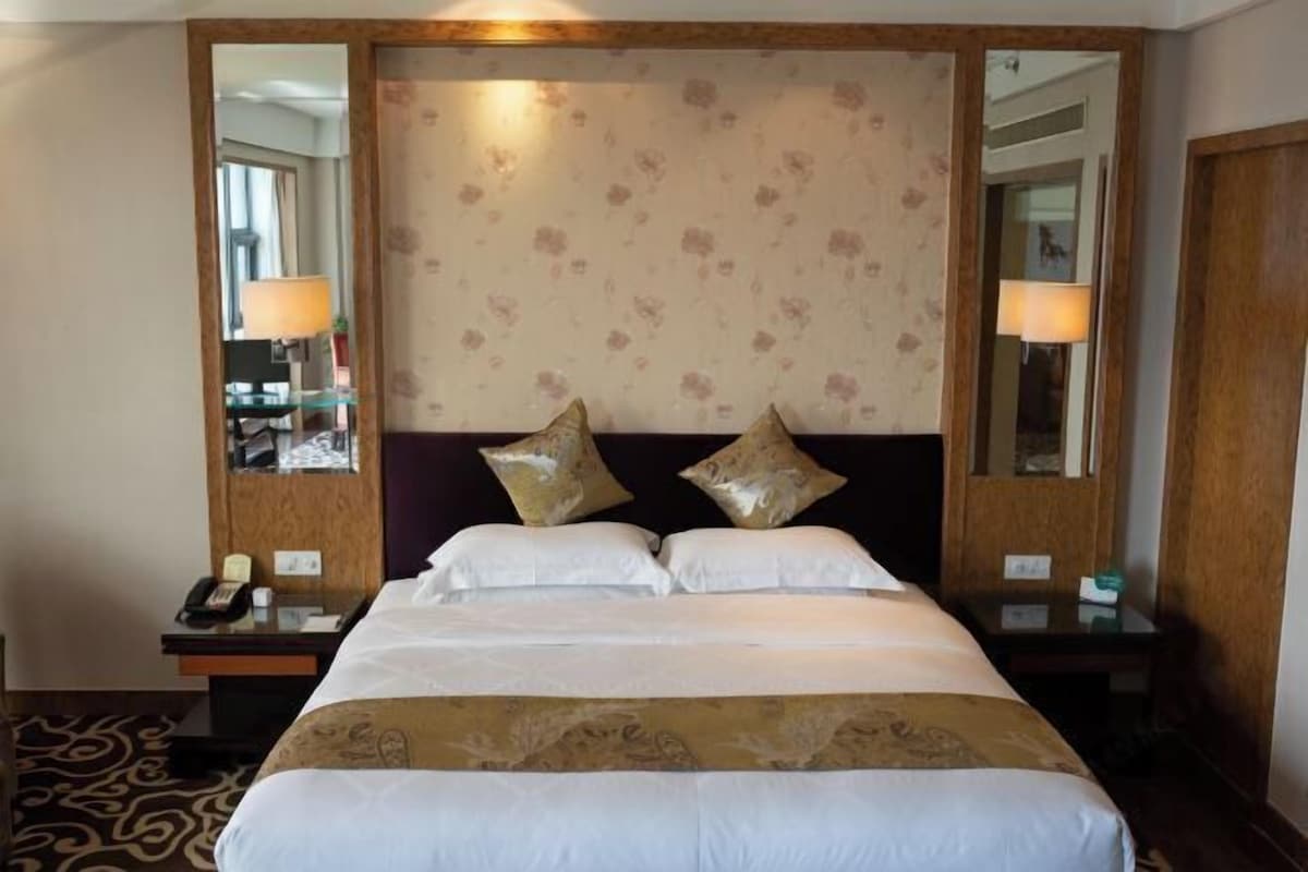 Une chambre d’hôtel avec un grand lit, deux tables de chevet, un miroir et une tête de lit à motifs floraux.