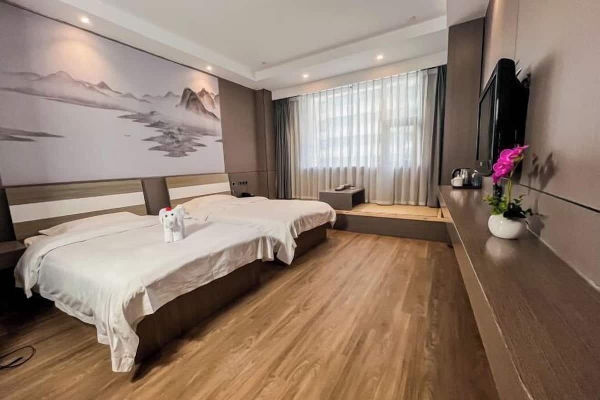 Een hotelkamer met twee bedden, een groot schilderij aan de muur, een televisie en een klein tafeltje met een plant.