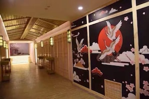 Un couloir orné de peintures murales traditionnelles japonaises, doté d’un plancher en bois et offrant une vue sur une pièce dont le sol est recouvert de tatamis.