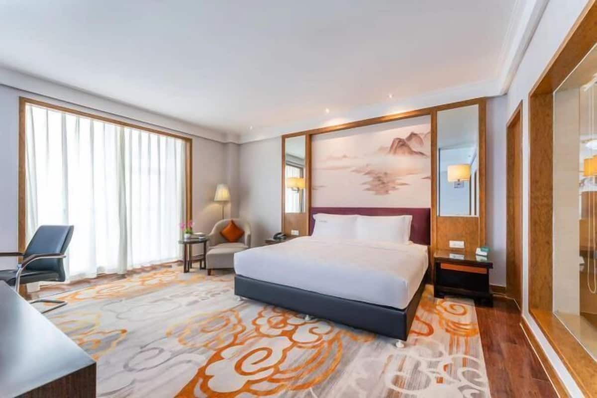 Een hotelkamer met een groot bed, een bureau, een stoel, een nachtkastje en een schilderij aan de muur.