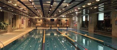 Ein großes Hallenbad mit mehreren Bahnen, einem Fliesenboden und einer Decke mit freiliegenden Balken und Leuchten.