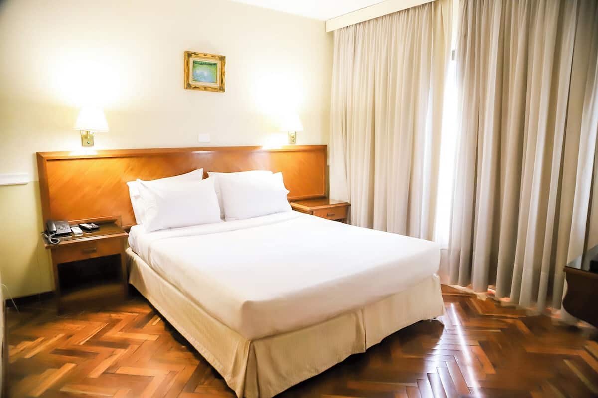 A hotel room with a large bed, wooden headboard, two bedside tables with lamps, a telephone, and a picture on the wall.