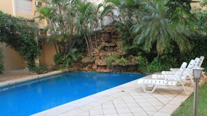 A swimming pool with a tiled deck, lounge chairs, and a rock waterfall. - Nobile Hotel Premier Hill (Asunción)