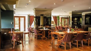 A restaurant with wooden tables and chairs, a bar area, and large windows with curtains. - Nobile Hotel Premier Hill (Asunción)