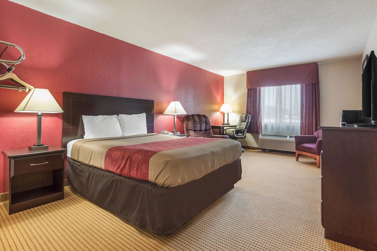 A hotel room with a large bed, two bedside tables, a desk, a chair, and a television.