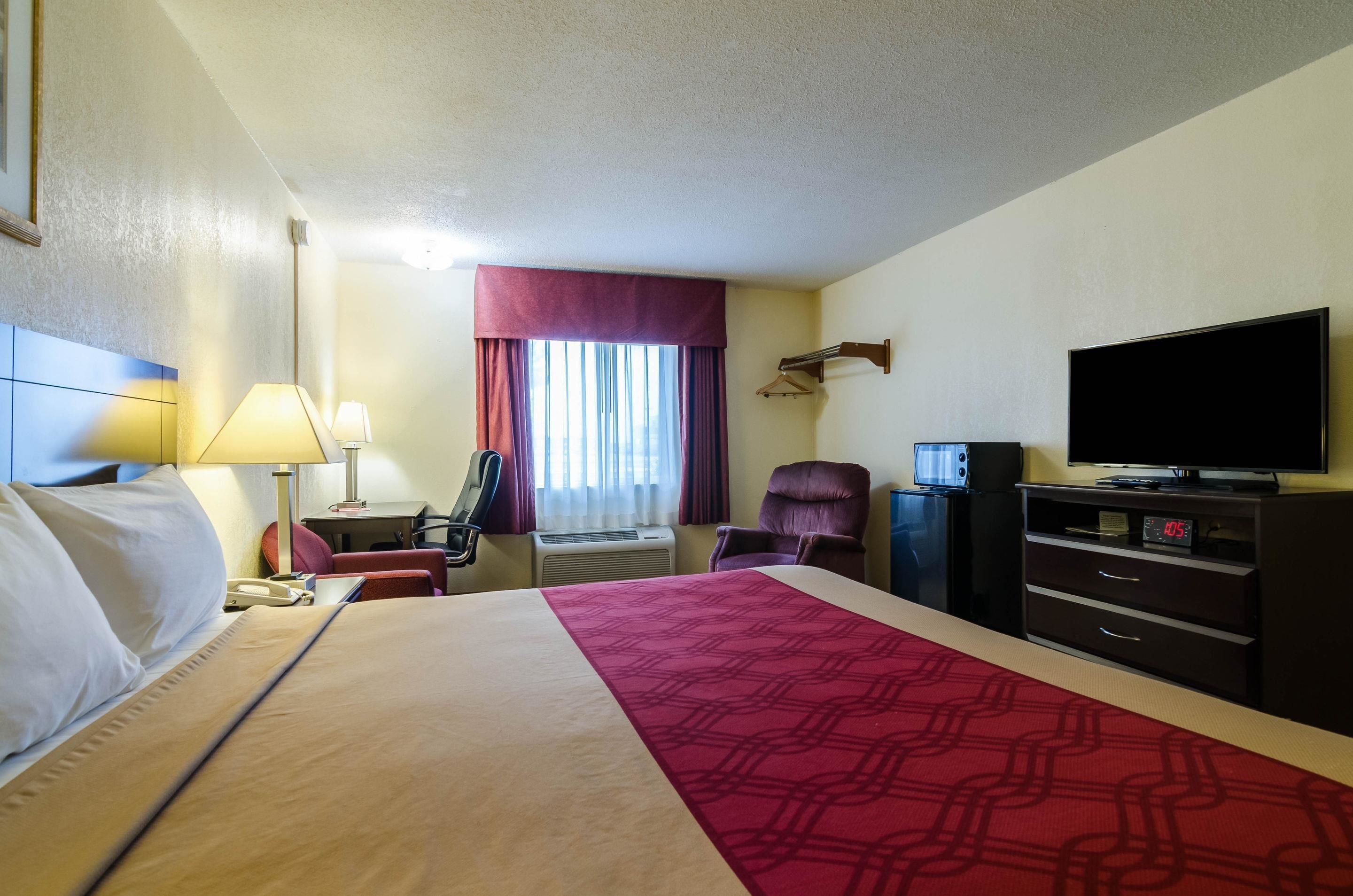 A hotel room with a bed, a desk with a lamp, a chair, a TV, and a dresser.