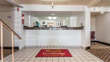 Un'area reception con pavimento piastrellato, una scrivania della reception, un quadro incorniciato appeso al muro e un tappeto rosso con la scritta 'EconoLodge Lexington, NE'.
