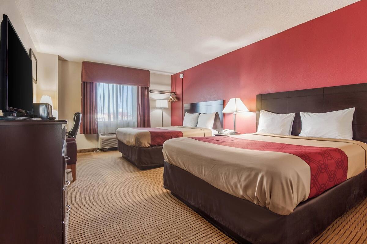 A hotel room with two beds, a TV, a desk, and a window with curtains.
