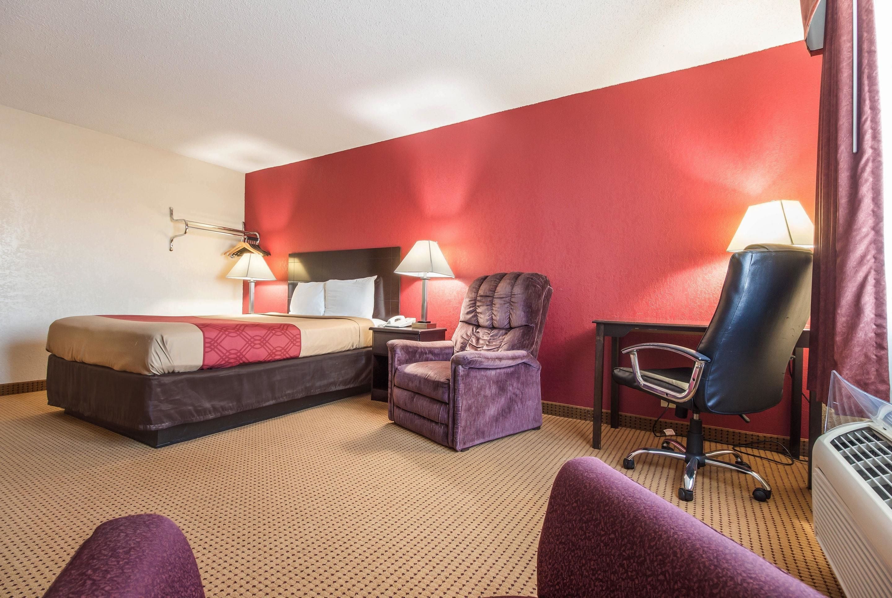 Una habitación de hotel con cama, dos sillas, un escritorio y una lámpara.