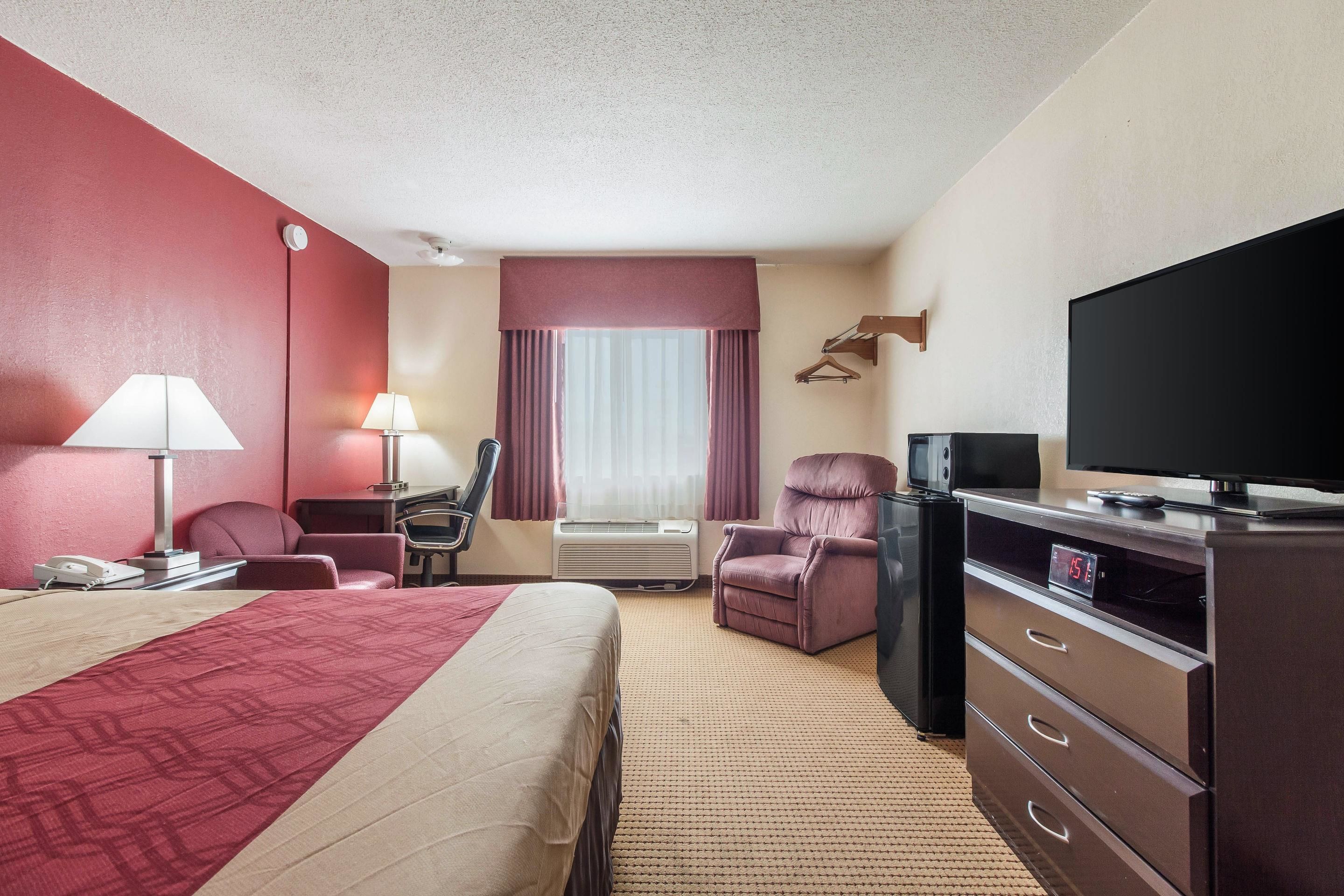 A hotel room with a bed, a desk with a lamp, a chair, a TV, and a dresser.
