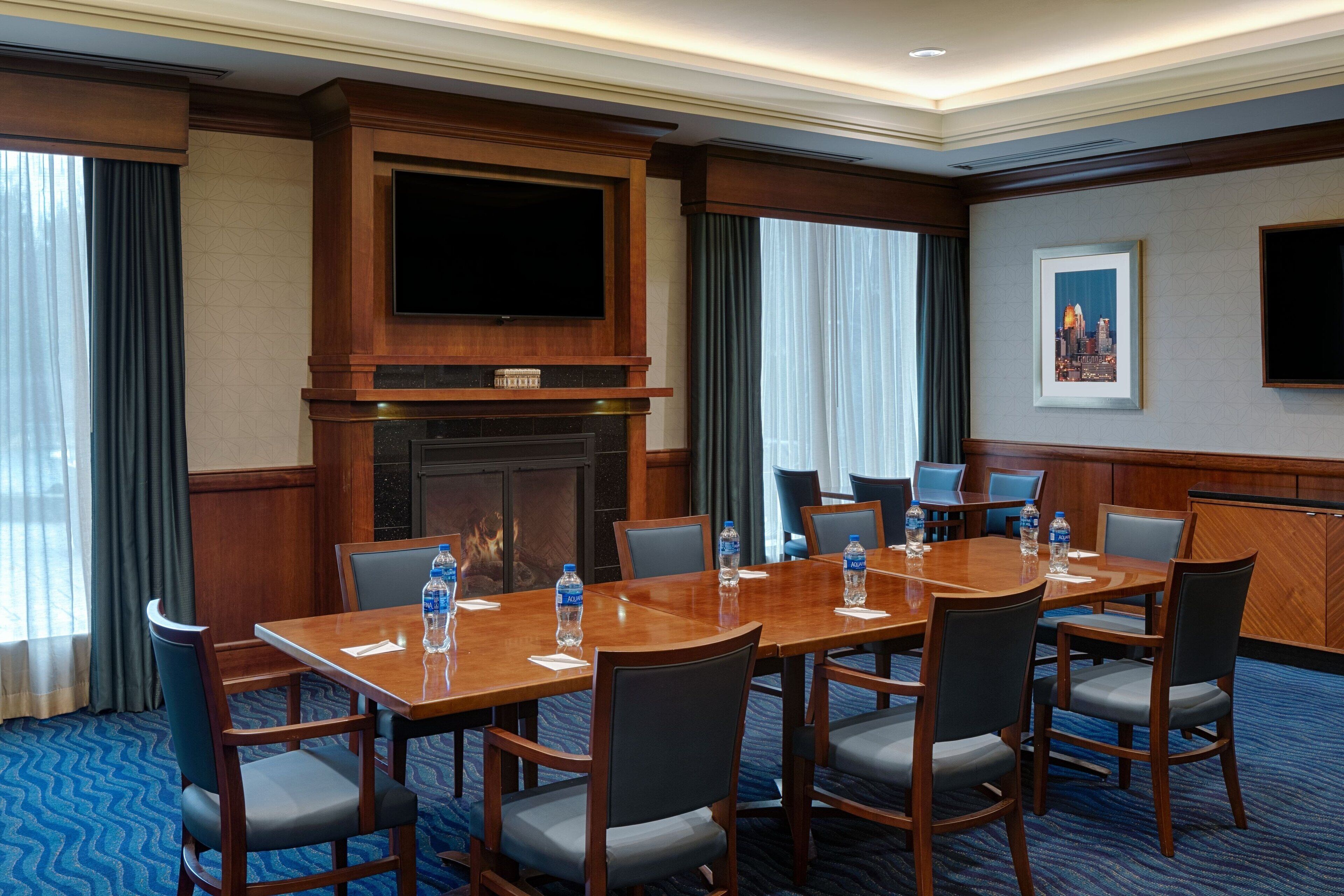 Een congreszaal met een grote houten tafel, stoelen, een open haard, een flatscreen-tv en een lijst met een stadsgezicht.