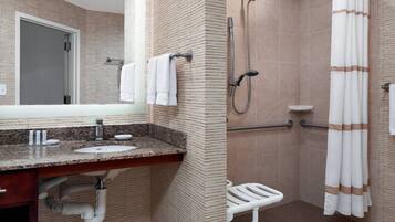 Un baño con lavamanos de encimera de granito, un espejo, ducha con cabezal de ducha manual y un toallero blanco.