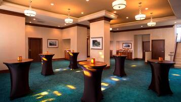 A spacious room with multiple round tables, recessed lighting, and a carpeted floor.
