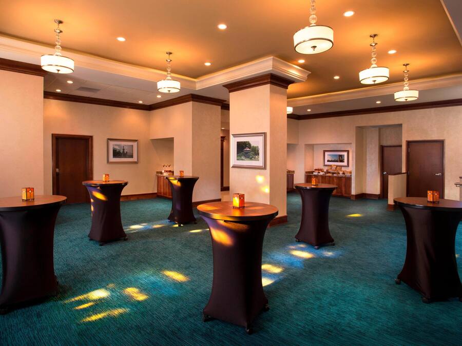 A spacious room with multiple round tables, recessed lighting, and a carpeted floor.