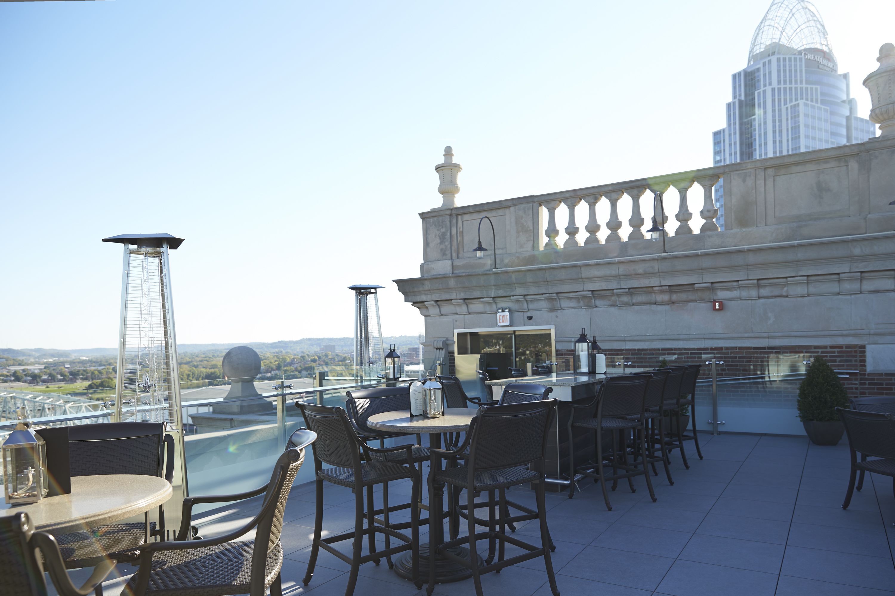 A rooftop terrace with outdoor seating, a bar area, and a view of a cityscape.