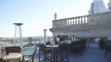 A rooftop terrace with outdoor seating, a bar area, and a view of a cityscape.