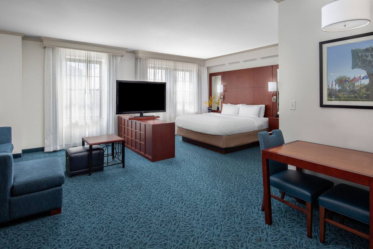 A hotel room with a large bed, a TV, a desk with two chairs, and a dining table.